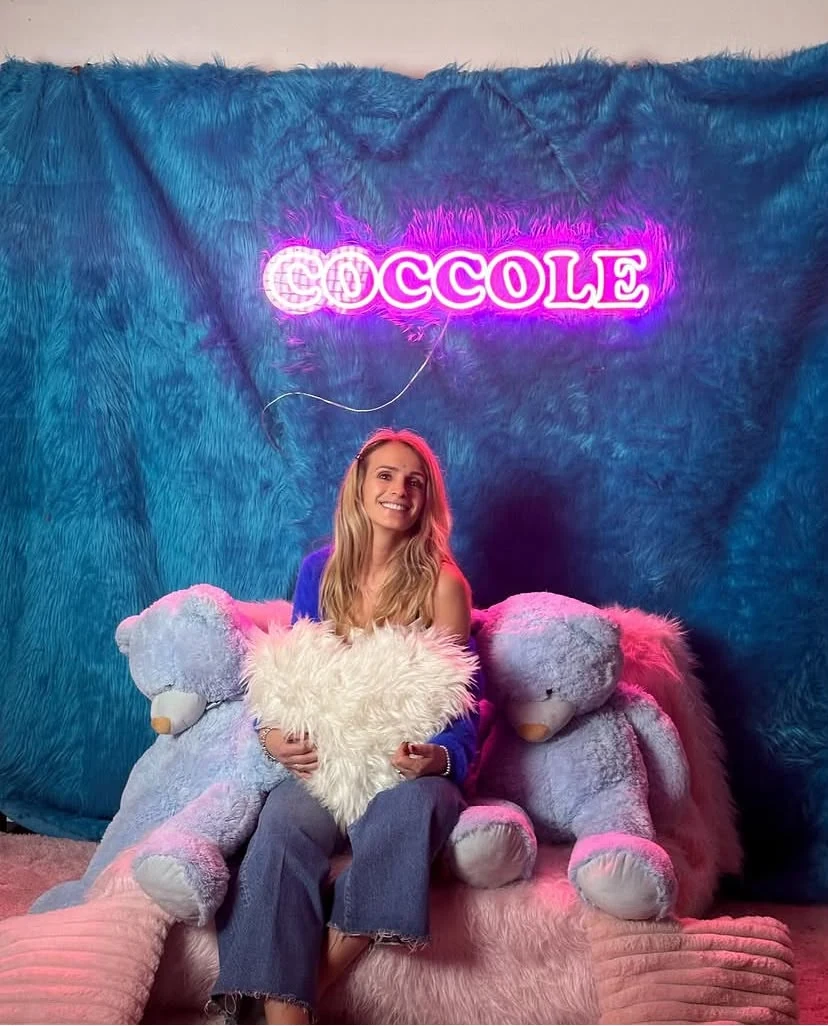 Dorina seduta tra peluche con scritta luminosa Coccole